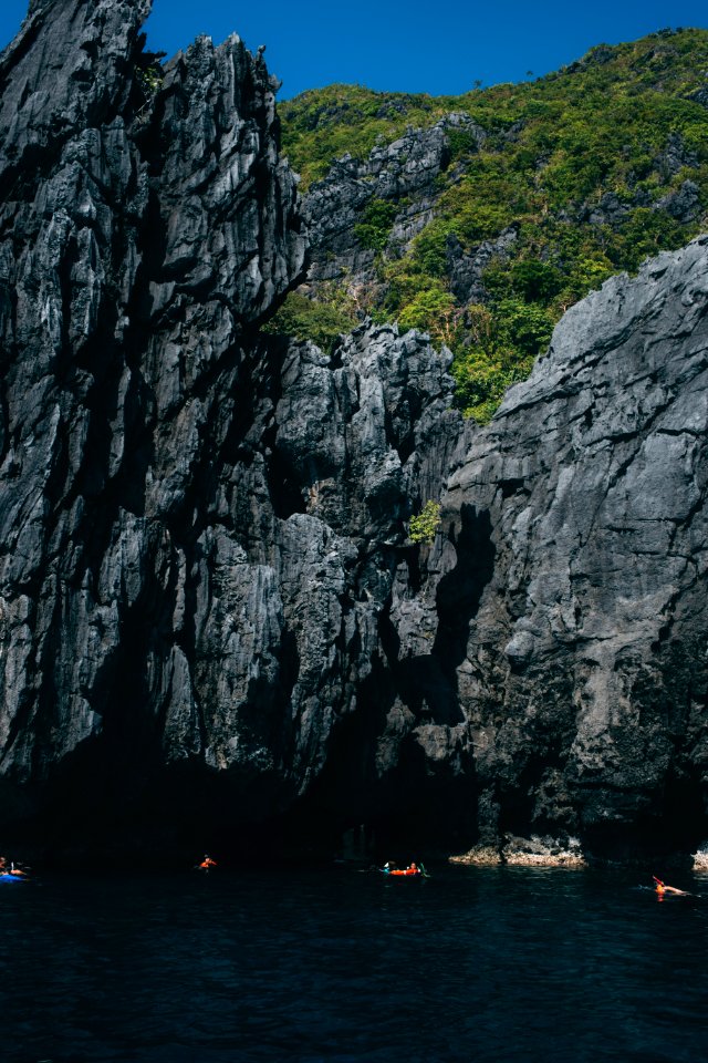 people on sea outside rock cave