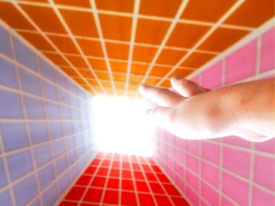 A hand reaching up to a sky-lit window in a room surrounded by four different color walls with box patterns.