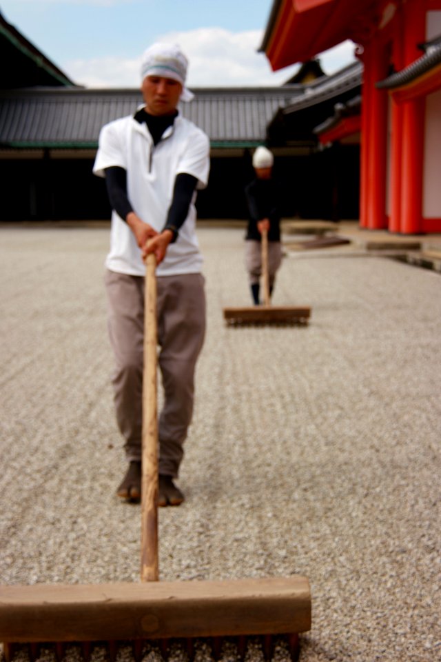 Two Asian men sweeping at their temple's courtyard.