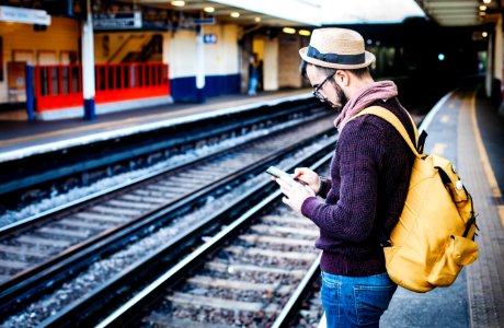 man using phone while standing in front of train rail during daytime photo