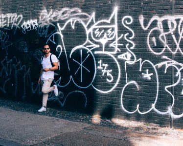 man wearing white crew-neck T-shirt leaning on black wall with white graffiti photo