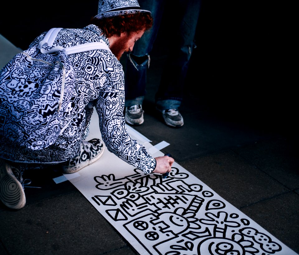 man drawing on white paper while kneeling at daytime