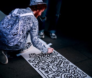 man drawing on white paper while kneeling at daytime photo