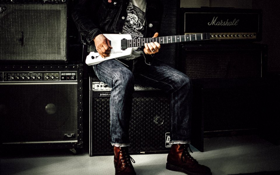 man wearing blue denim jeans playing white and black electric guitar sitting on black guitar amplifier photo