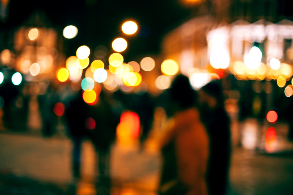 An out-of-focus look at people walking outside in a town at night with with blurs of dotted light all around