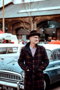 man wearing plaid button-up coat in front of classic car