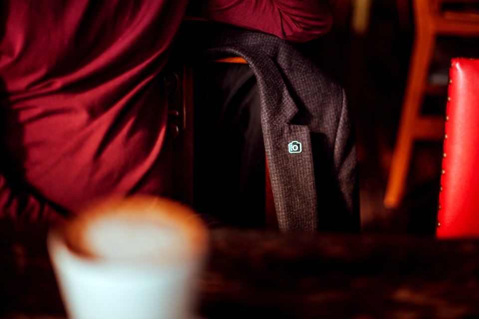 A blazer with an Unsplash pin, hanging on a chair at a cafe table