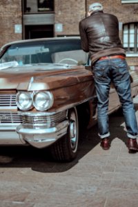 man in blue denim pants standing beside brown car photo