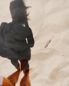 The shadow of a woman standing in the sand on a beach.