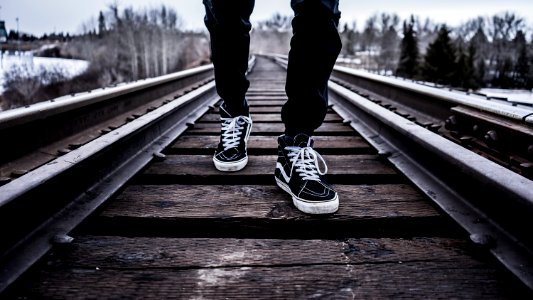 person wearing pair of black-and-white Vans Old Skool shoes walking on brown train tracks during winter photo