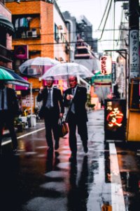 two men in black suit holding transparent umbrellas walking in the street photo