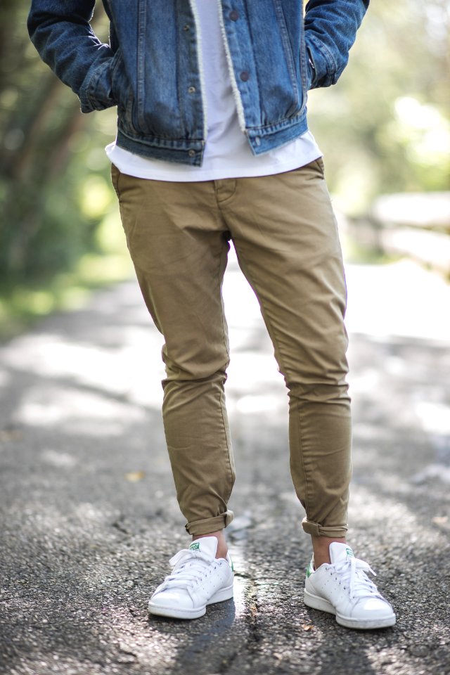 man wearing brown fitted jeans and sneakers standing on road at daytime