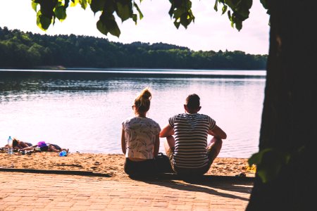 men and woman sitting on pavement facing body of water photo