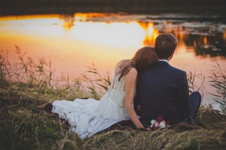 sitting woman leaning on man's shoulder facing lake during golden hour photo