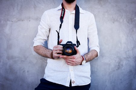 man in white dress shirt holding Canon DSLR camera photo