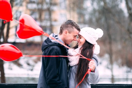 A man and woman smiling while touching face to face, as the girl holds red heart shaped balloons. photo