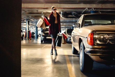 woman carrying shopping paper bags walking towards beige car inside parking lot photo