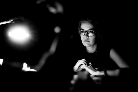 grayscale photo of a woman wearing eyeglasses sitting in front of table photo