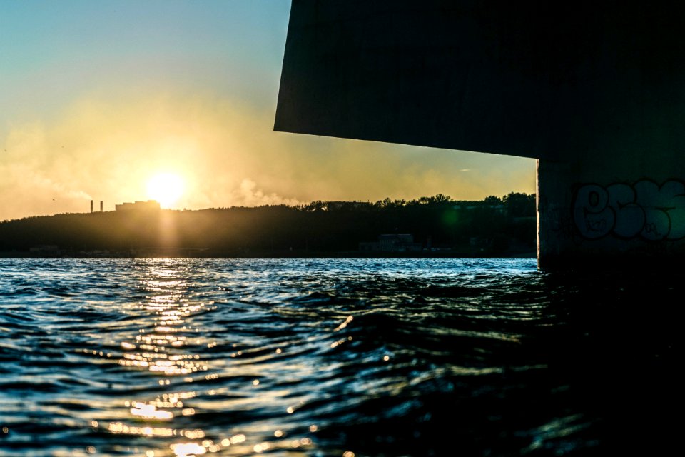 low angle photography of sun behind building on hill over the sea photo