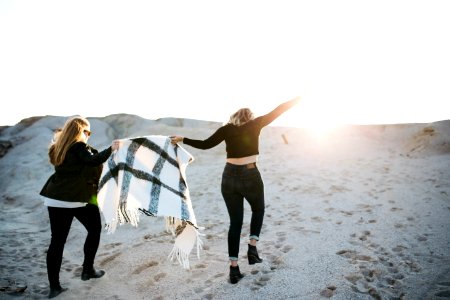 vignette photography of two woman holding scarf walking on sand photo