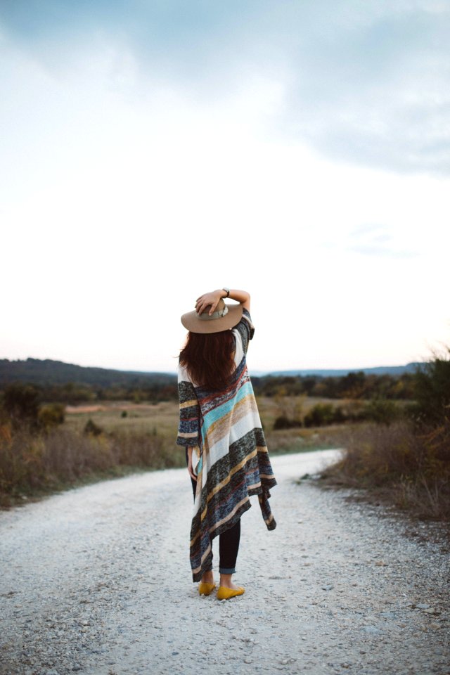 standing woman holding her hat at the middle of the road during day