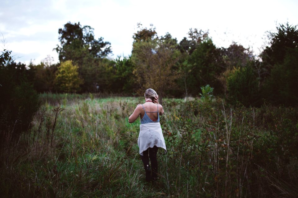 woman walking on green field surrounded with tall and green trees