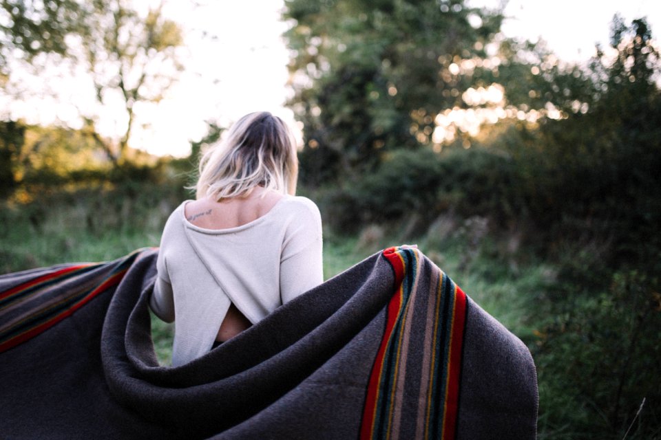 standing woman holding gray blanket surrounded by green grass