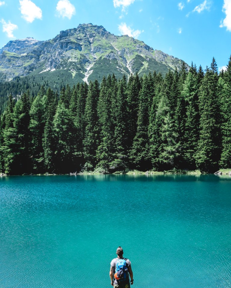 man looking through on lake with pine trees under blue sky