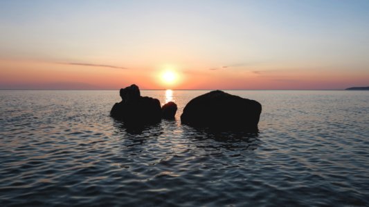 silhouette of rocks on body of water during golden hour photo