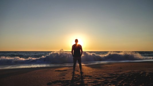 man in black shirt standing on beach during sunset photo