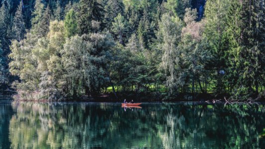 two people on red boat on water near trees during daytime photo