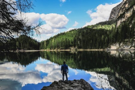 man in blue jacket standing on rock near lake during daytime photo