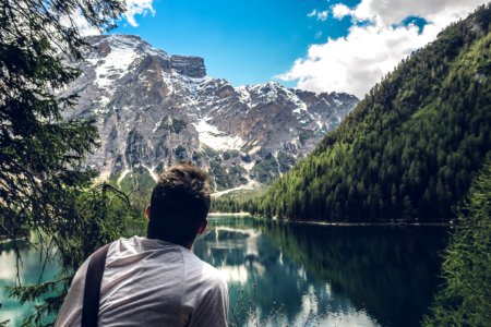 man in white shirt sitting on rock looking at lake and mountains during daytime photo