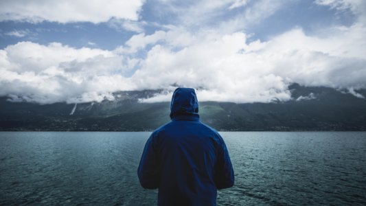 person wearing blue hoodie standing infront of body of water photo