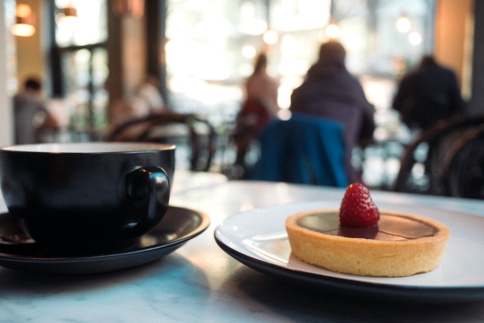 pie with raspberry on top near black and white ceramic cup and saucer on table photo