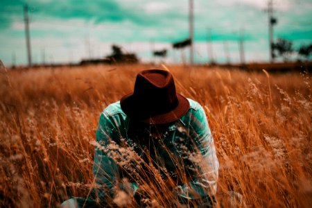 man squatting surrounded by brown grass during daytime photo