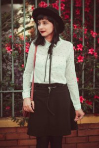 woman in white dress shirt and black skirt standing near fence with red flowers photo