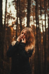 portrait photography of woman wearing black coat surrounded by forest trees during daytime photo