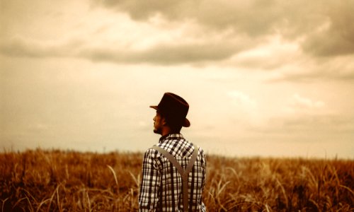 man wearing black hat standing on brown field during daytime photo