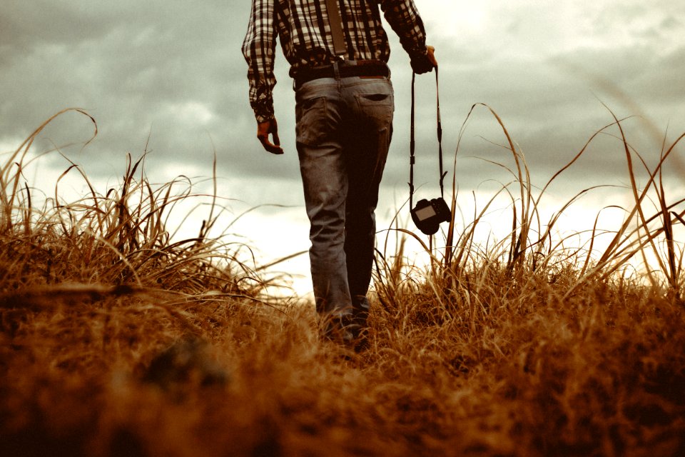 man holding DSLR camera walking through brown grass
