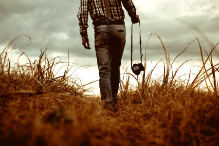 man holding DSLR camera walking through brown grass photo