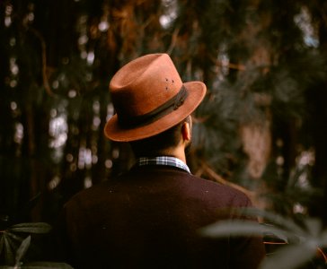 person wearing brown fedora hat facing trees