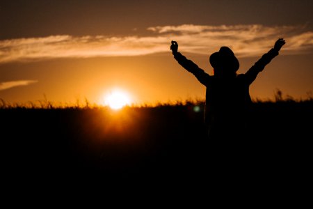 silhouette of person raising his two arms during sunrise