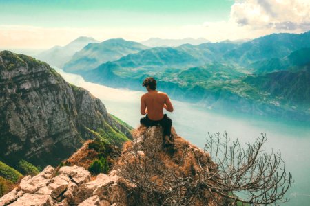 man seating on top of cliff in front of mountains photo