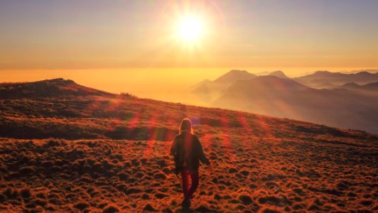 woman in blue jacket walking on desert during sunset photo