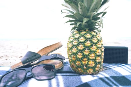 green and yellow pineapple besides black slide slippers and sunglasses photo