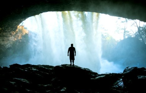 man standing on rock near cave