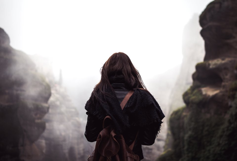 woman carrying brown backpack standing in front of mountains during daytime