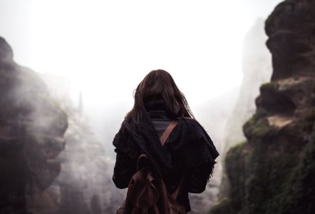 woman carrying brown backpack standing in front of mountains during daytime photo