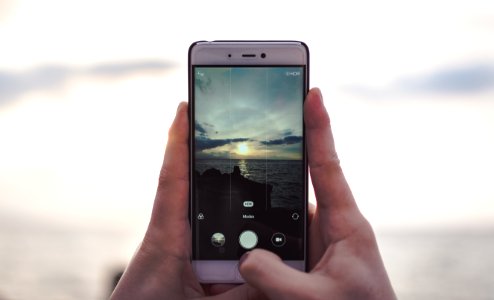 A person taking a picture of the ocean under clouds.
